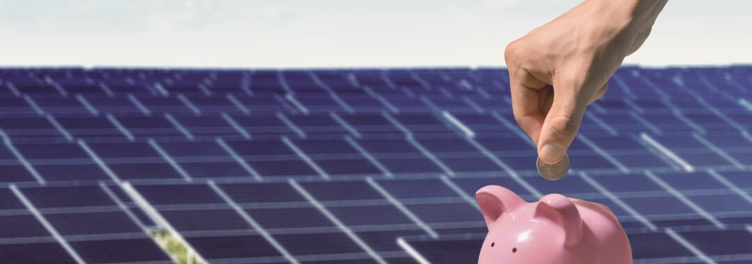 Putting money into piggy bank in front of solar panels